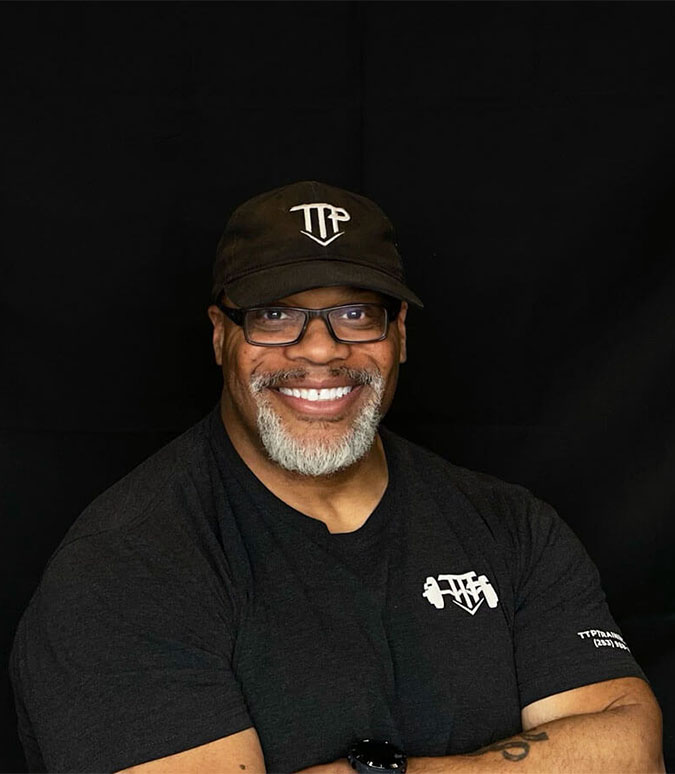 Turk, owner of TTP Fitness smiling and wearing a TTP shirt and hat.