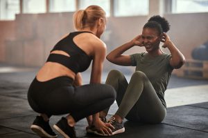 Woman smiling while doing sit-ups with a workout partner on the floor of a gym