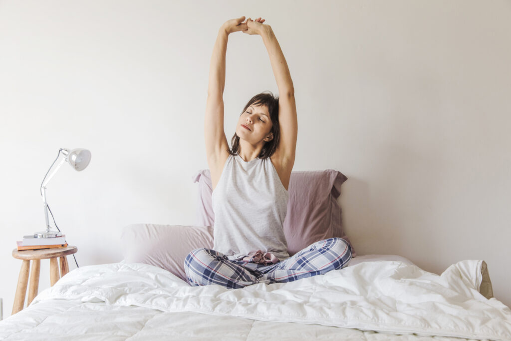 Woman stretching in bed after waking up, showing connection between sleep and exercise